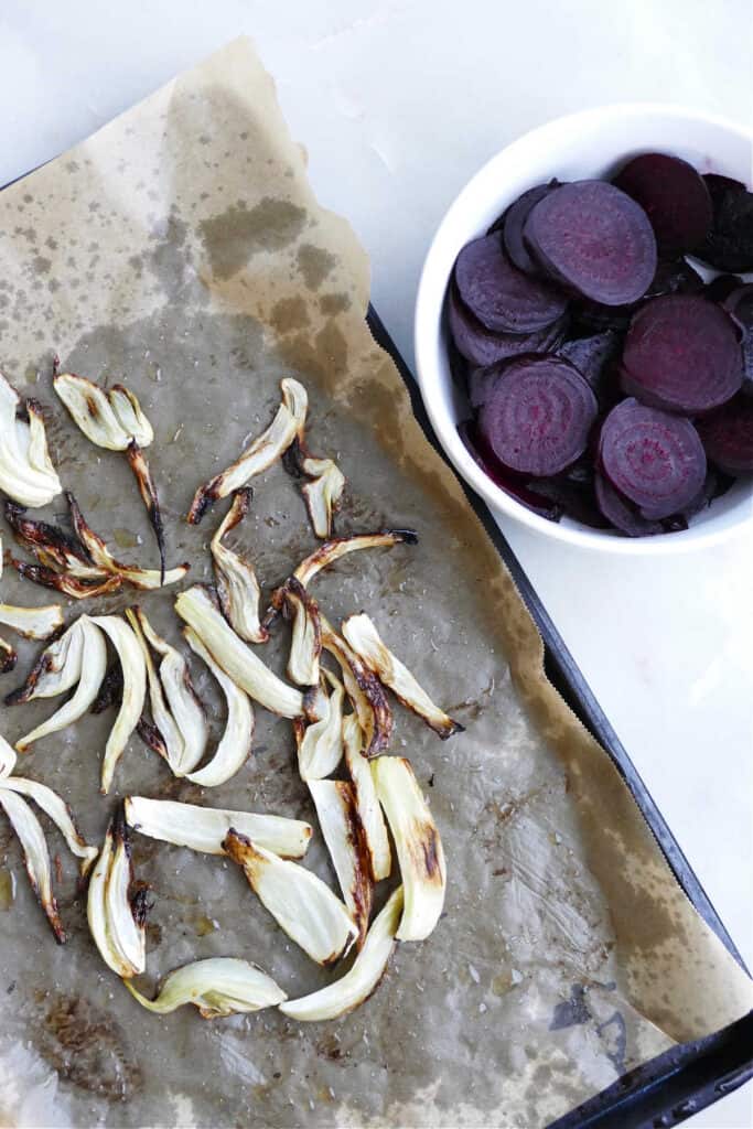 roasted fennel on a baking sheet and sliced beets in a bowl on a counter