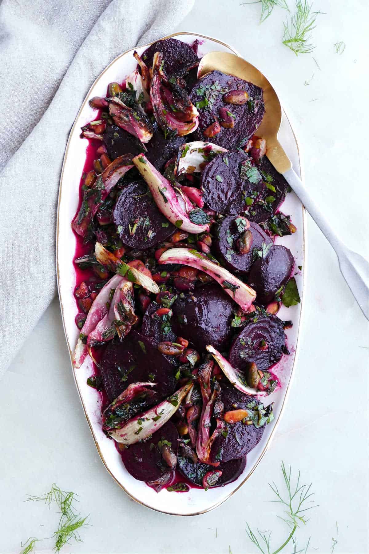 beet and fennel salad on an oval tray with a gold and silver serving spoon