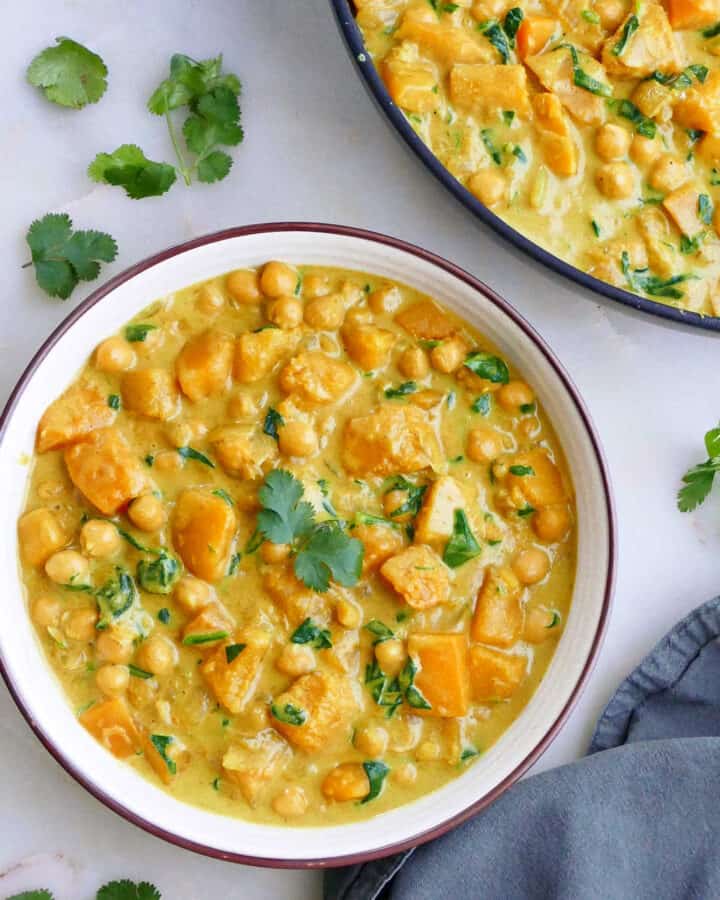 butternut squash and chickpea curry in a serving bowl next to a skillet filled with the curry