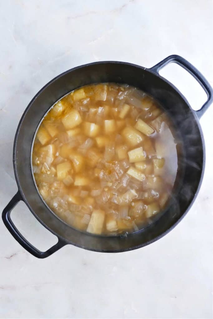 celeriac, onion, garlic, and parsnip cooking in vegetable broth in a soup pot