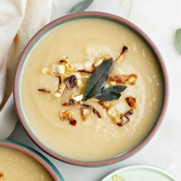 bowl of celeriac and parsnip soup topped with fried sage and crispy parsnips next to toppings