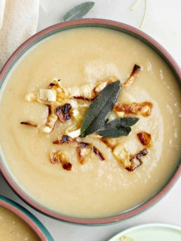 bowl of celeriac and parsnip soup topped with fried sage and crispy parsnips next to toppings