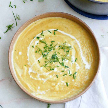 leek, potato, and fennel soup in a bowl with chives and heavy cream next to a napkin