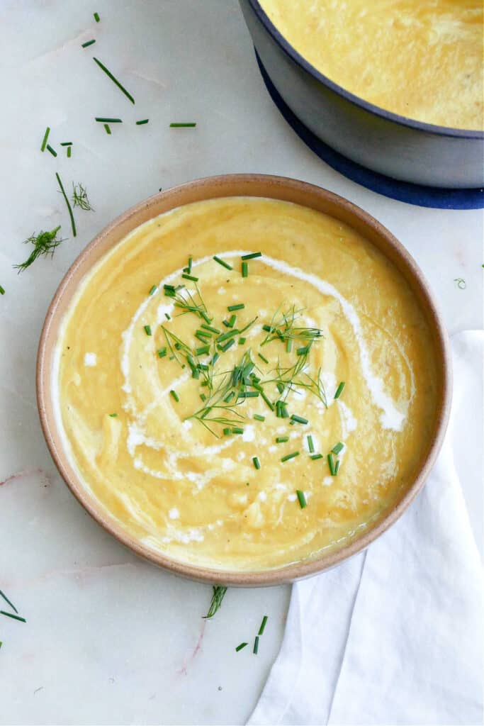 leek, potato, and fennel soup in a bowl with chives and heavy cream next to a napkin