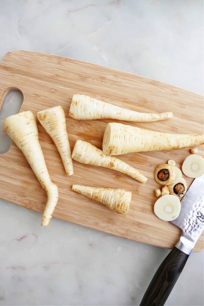 trimmed parsnips on a bamboo cutting board on a counter next to a chef's knife