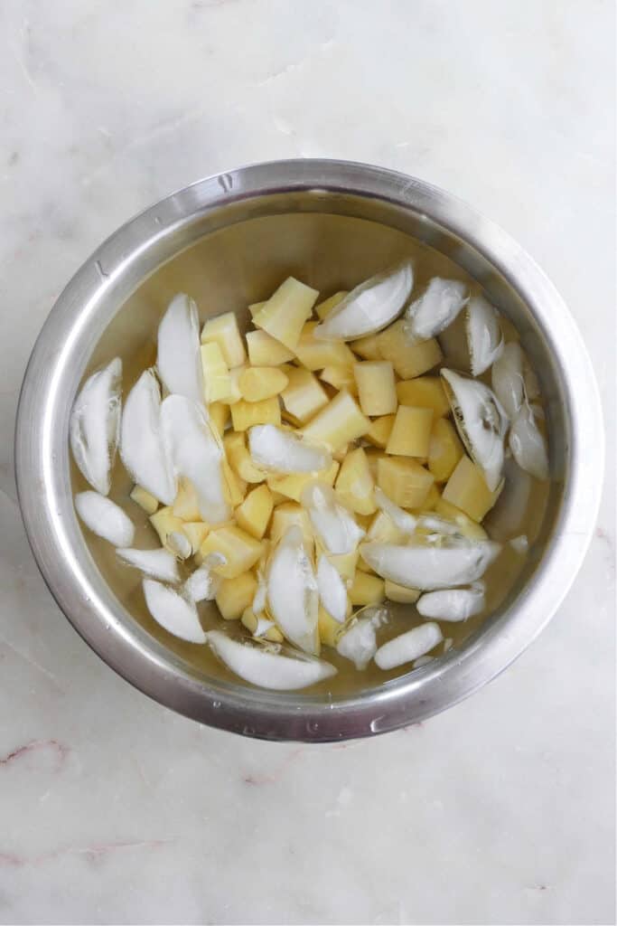 blanched parsnips cooling in a mixing bowl with ice water