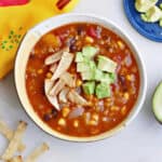 vegan lentil tortilla soup topped with tortilla strips and diced avocado