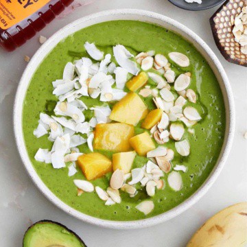 mango kale smoothie bowl topped with coconut, mango, and almonds surrounded by ingredients