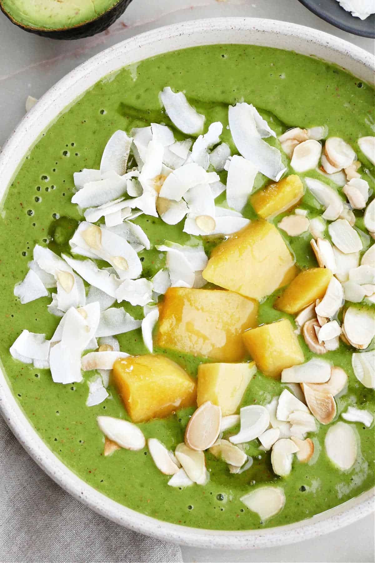 mango kale smoothie bowl topped with coconut, honey, mango, and almonds in a serving bowl
