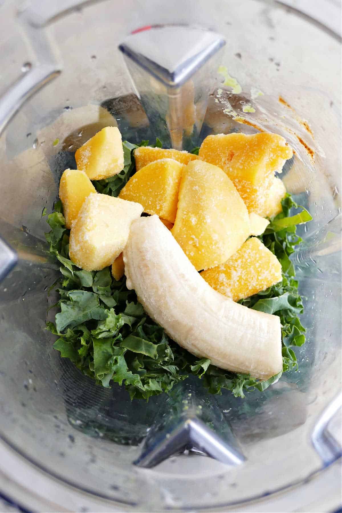 shredded kale, mango, banana, and other smoothie bowl ingredients in a blender