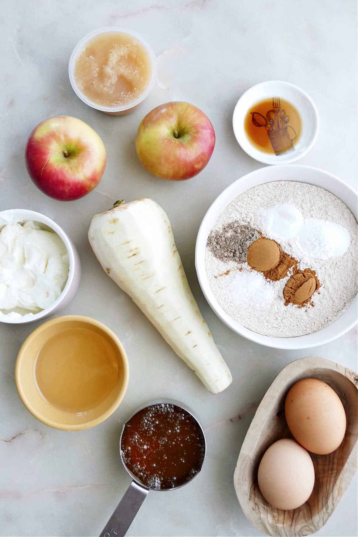 apples, applesauce, a parsnip, eggs, honey, oil, yogurt, and dry ingredients on a counter