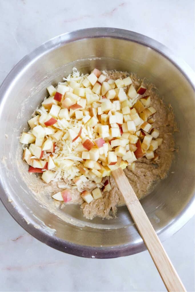 diced apples and shredded parsnips being mixed into a whole wheat muffin batter with a rubber spatula