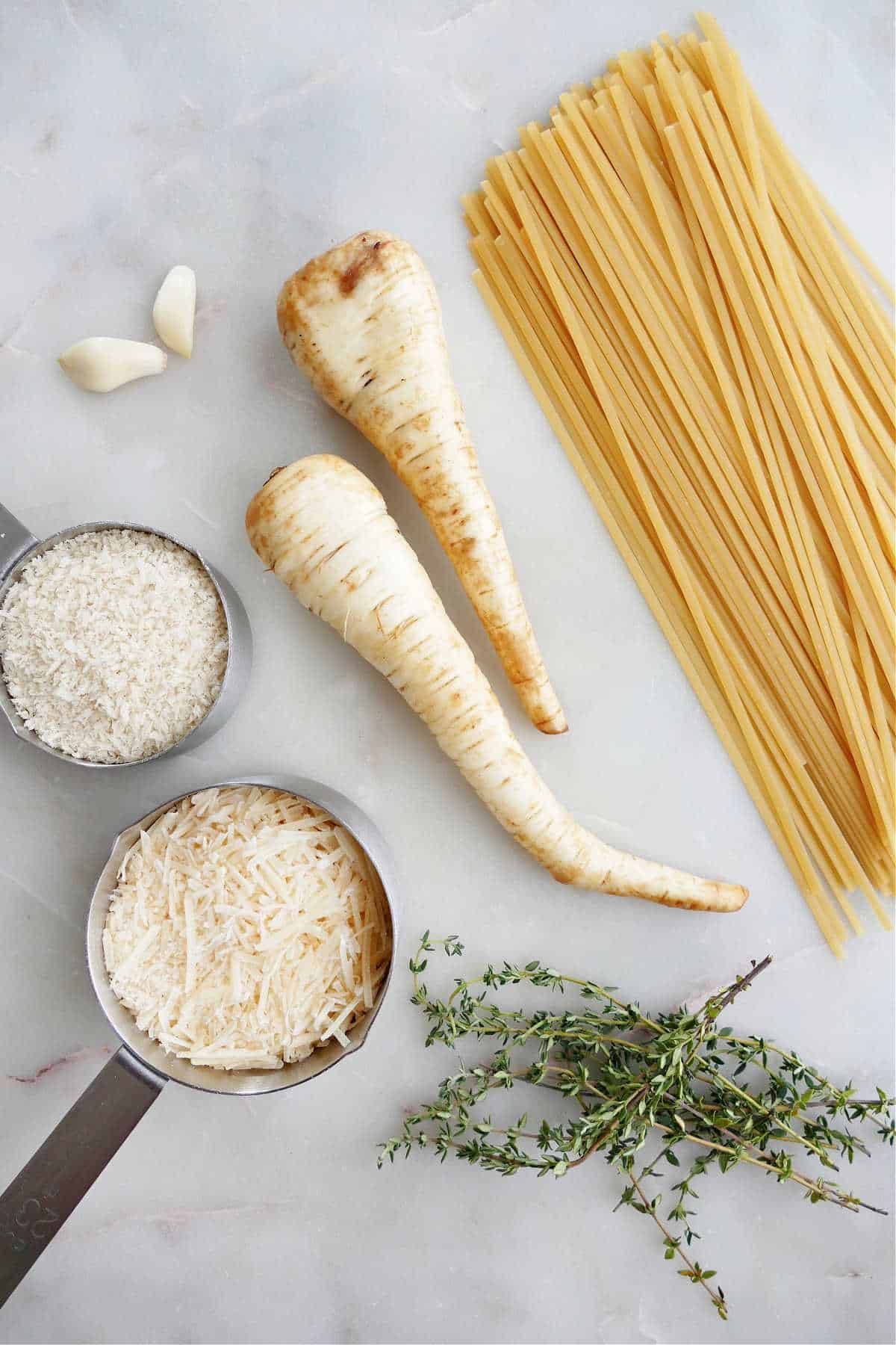 garlic, cheese, breadcrumbs, parsnips, linguine, and thyme next to each other on a counter
