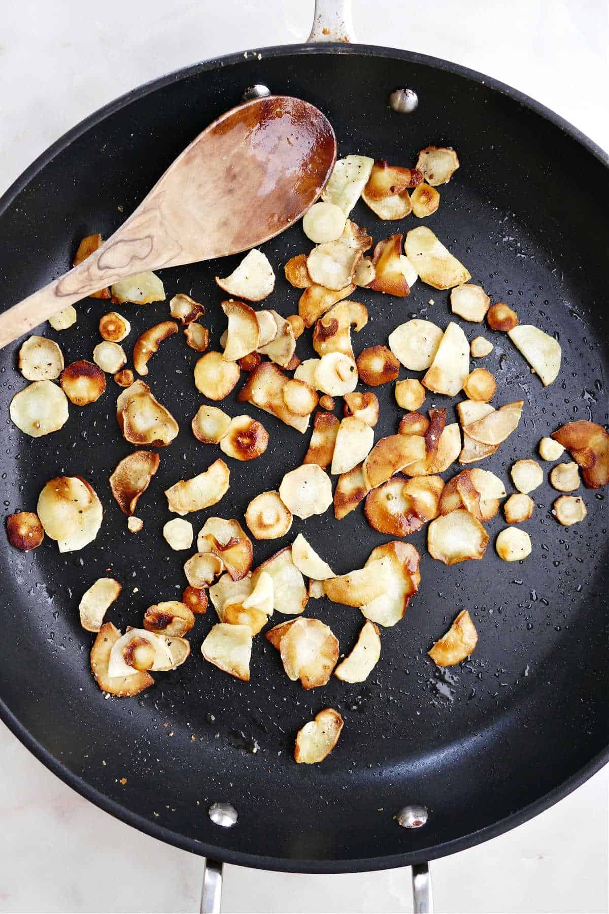 thinly sliced parsnips cooking in a skillet in olive oil