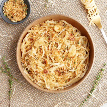 parsnip pasta topped with breadcrumbs in a serving bowl surrounded by ingredients