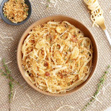 parsnip pasta topped with breadcrumbs in a serving bowl surrounded by ingredients