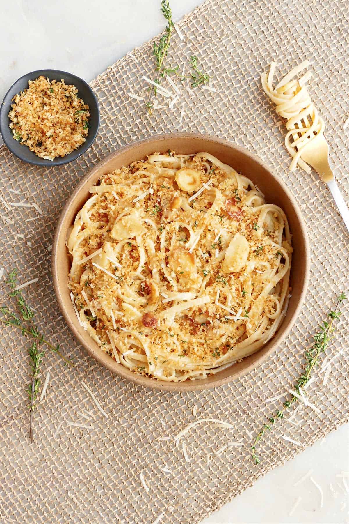 parsnip pasta topped with breadcrumbs in a serving bowl surrounded by ingredients