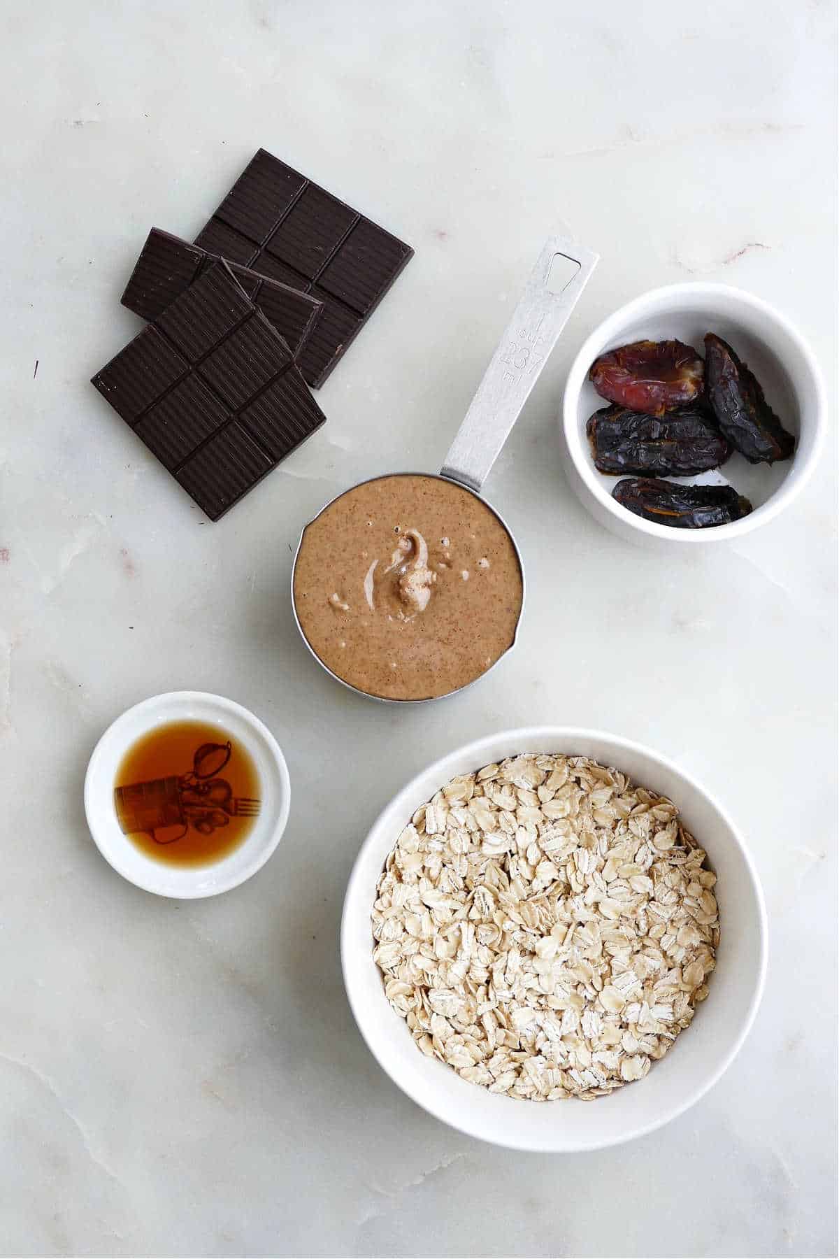 dark chocolate, almond butter, dates, vanilla, and oats next to each other on a counter