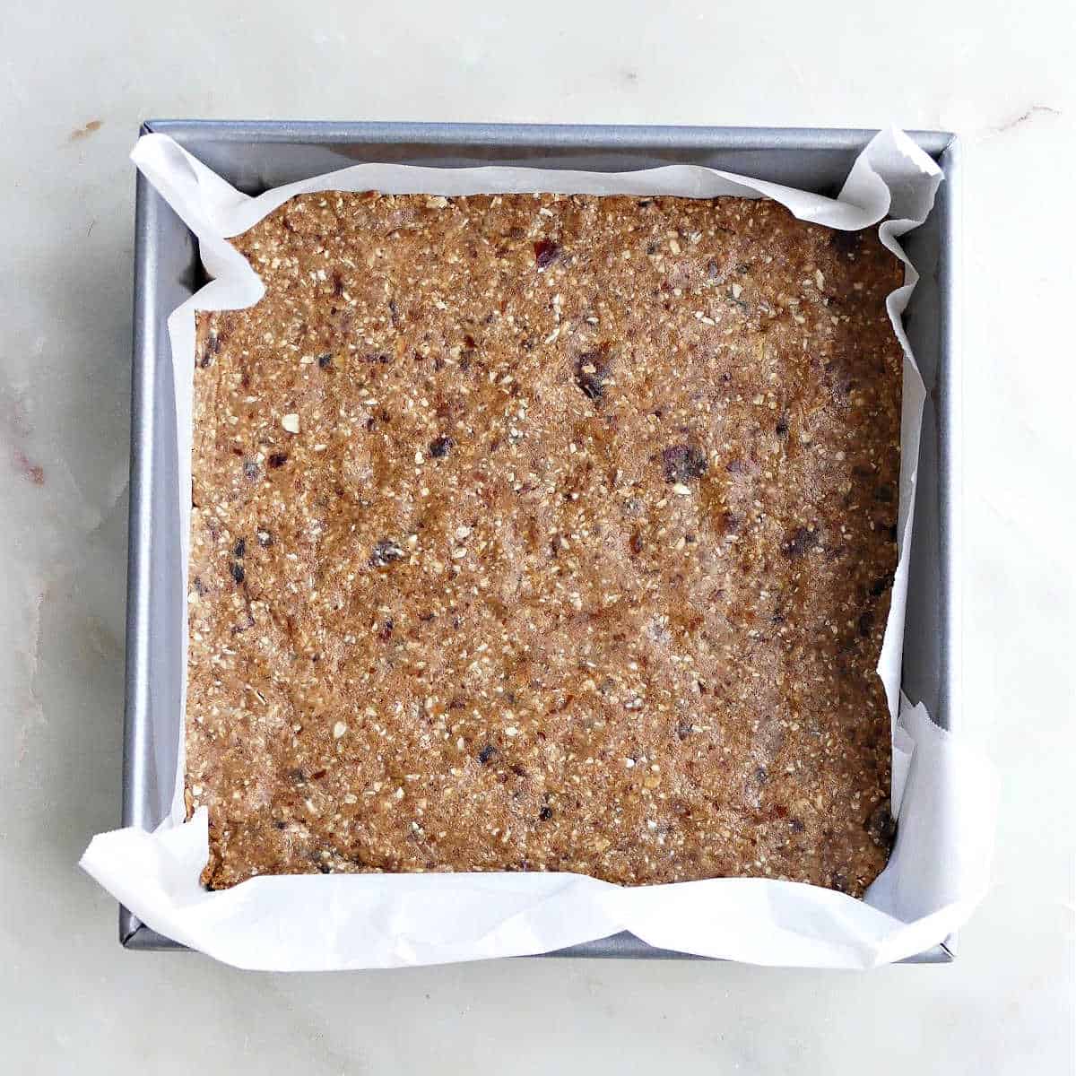 almond butter bar batter spread out in a square, lined baking dish