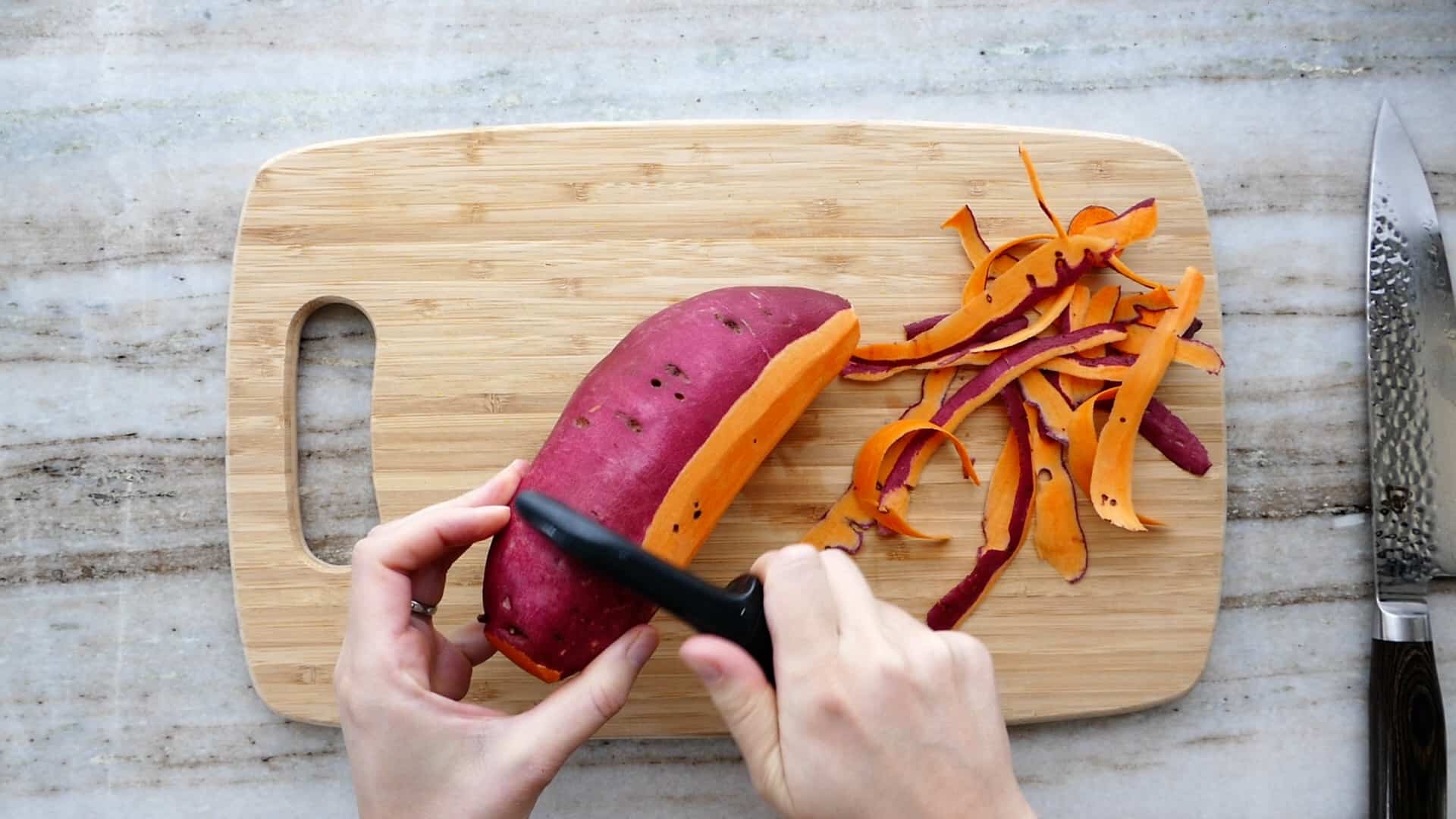 woman peeling a sweet potato with a swivel peeler over a cutting board