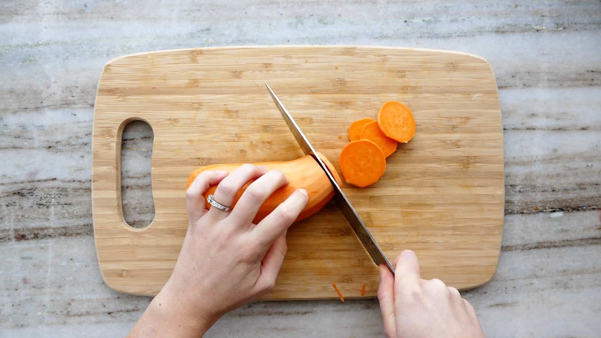 woman cutting sweet potato into rounds with a knife on a cutting board