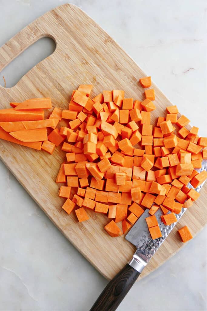 sweet potato cut into cubes on a bamboo cutting board with a knife