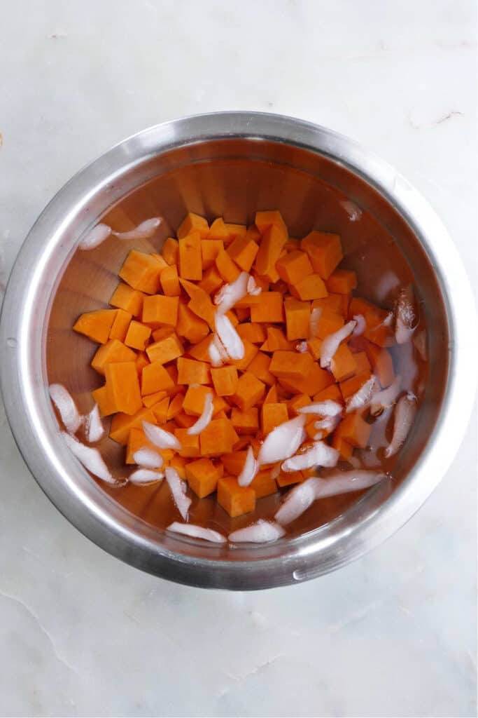 cubed sweet potatoes that are blanched and put into cold water in a bowl