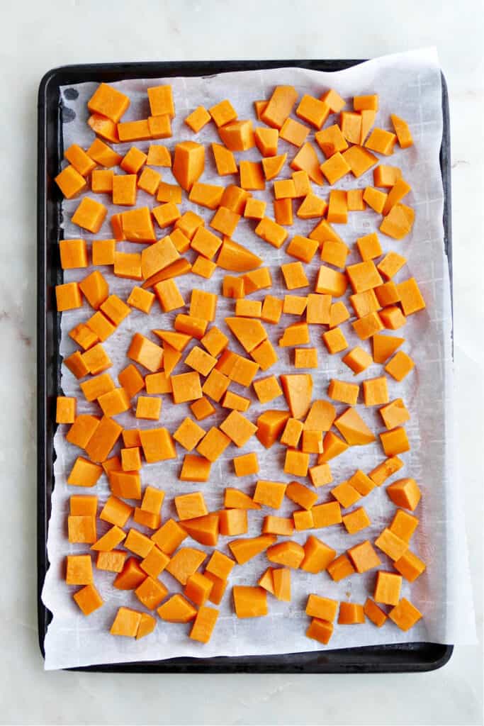 cubed sweet potatoes spread out on a lined baking sheet before freezing