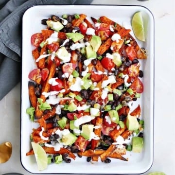 loaded sweet potato fries topped with avocado and Greek yogurt sauce on a serving tray