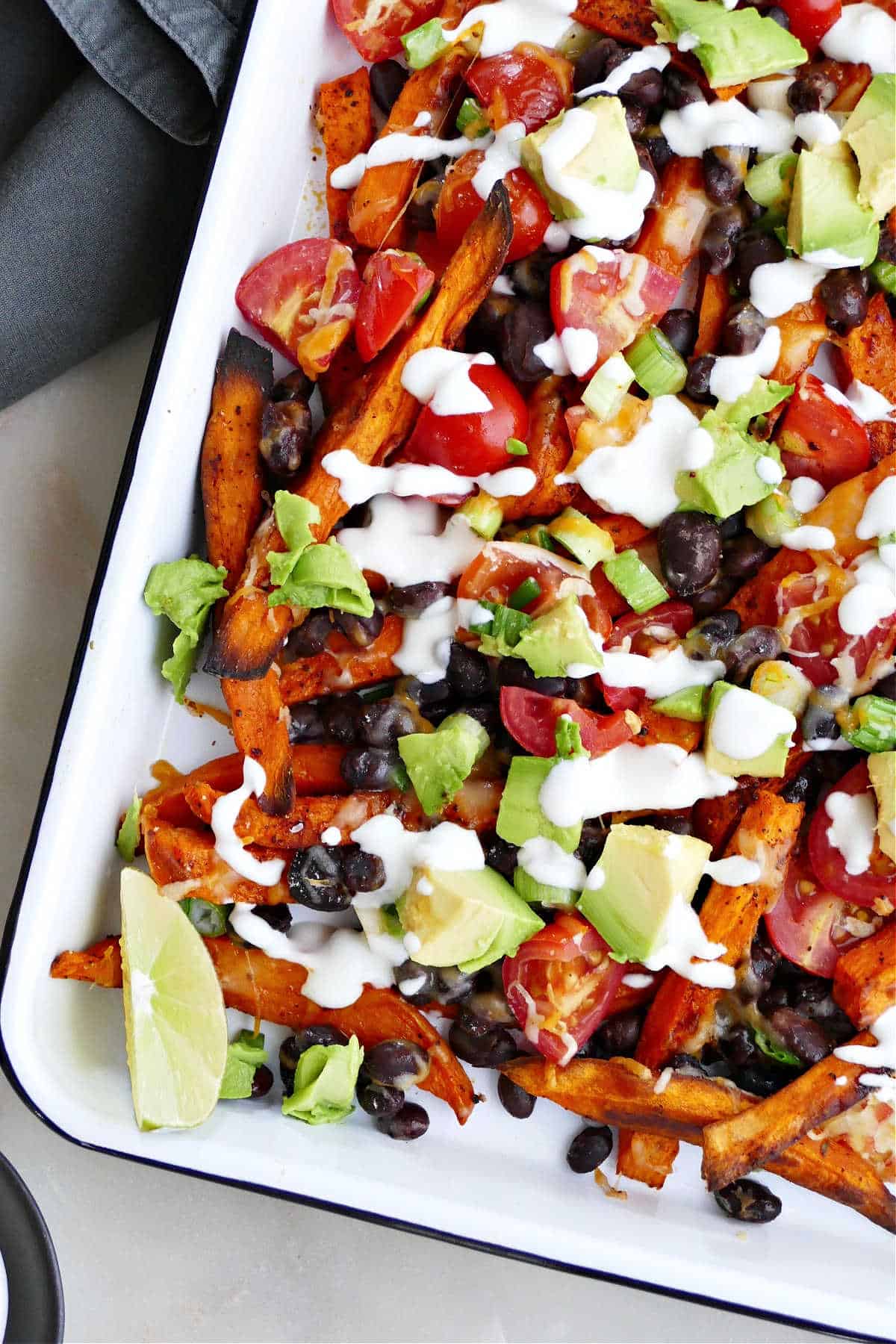 sweet potato fries with toppings on a serving tray with lime wedges