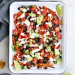 loaded sweet potato fries topped with avocado and Greek yogurt sauce on a serving tray