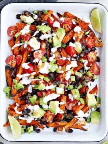 loaded sweet potato fries topped with avocado and Greek yogurt sauce on a serving tray