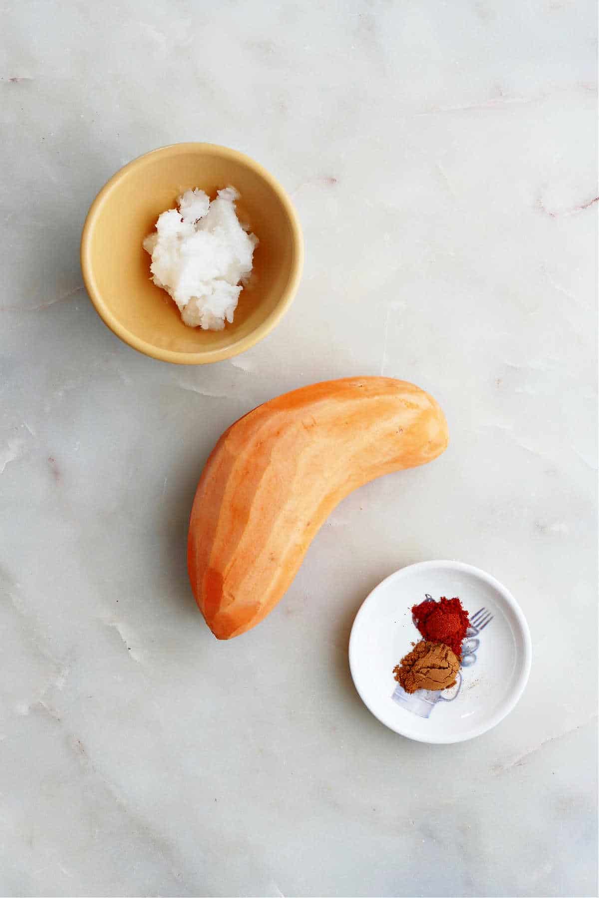 a peeled sweet potato next to coconut oil and seasonings on a counter