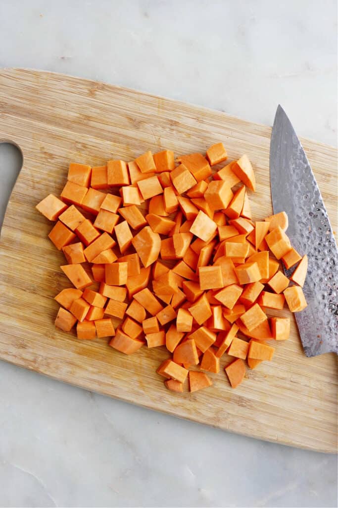 a sweet potato diced into cubes on a bamboo cutting board with a knife