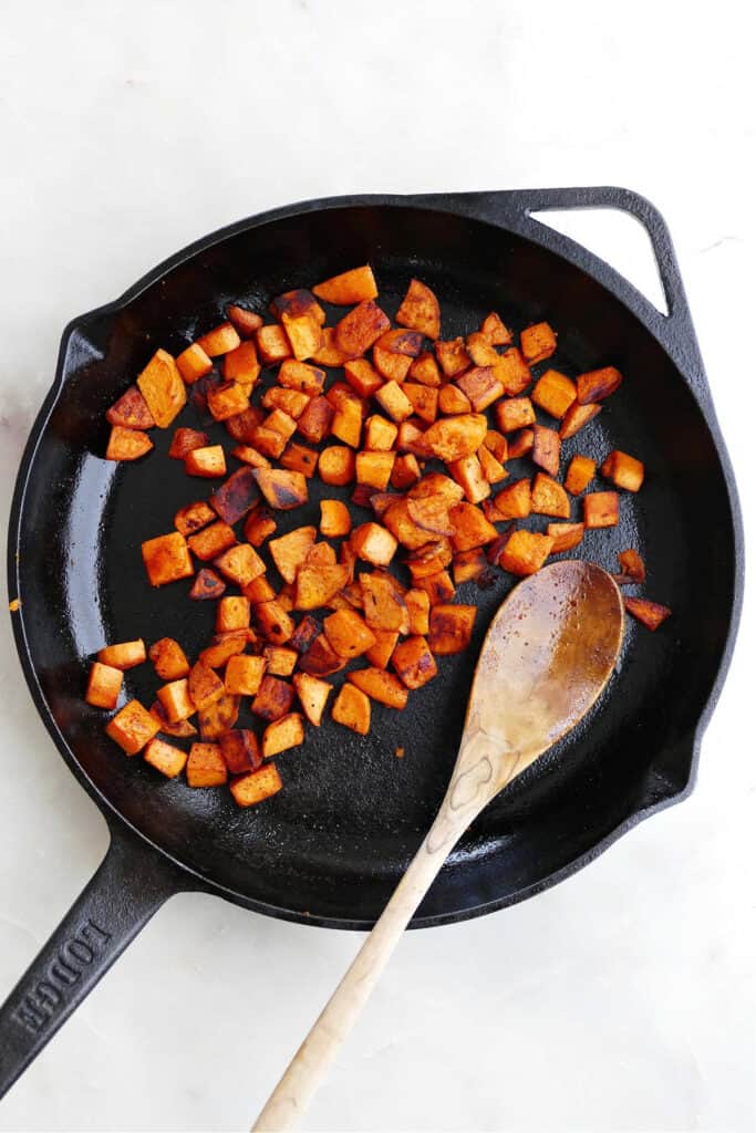 sweet potato cubes in a cast iron skillet being sauteed with a spoon