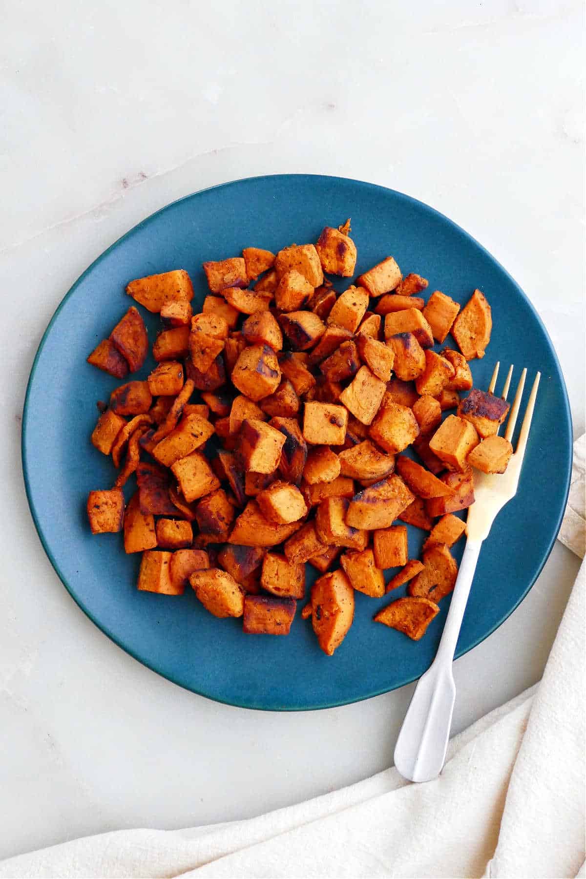 sauteed sweet potatoes on a serving plate with a small gold fork