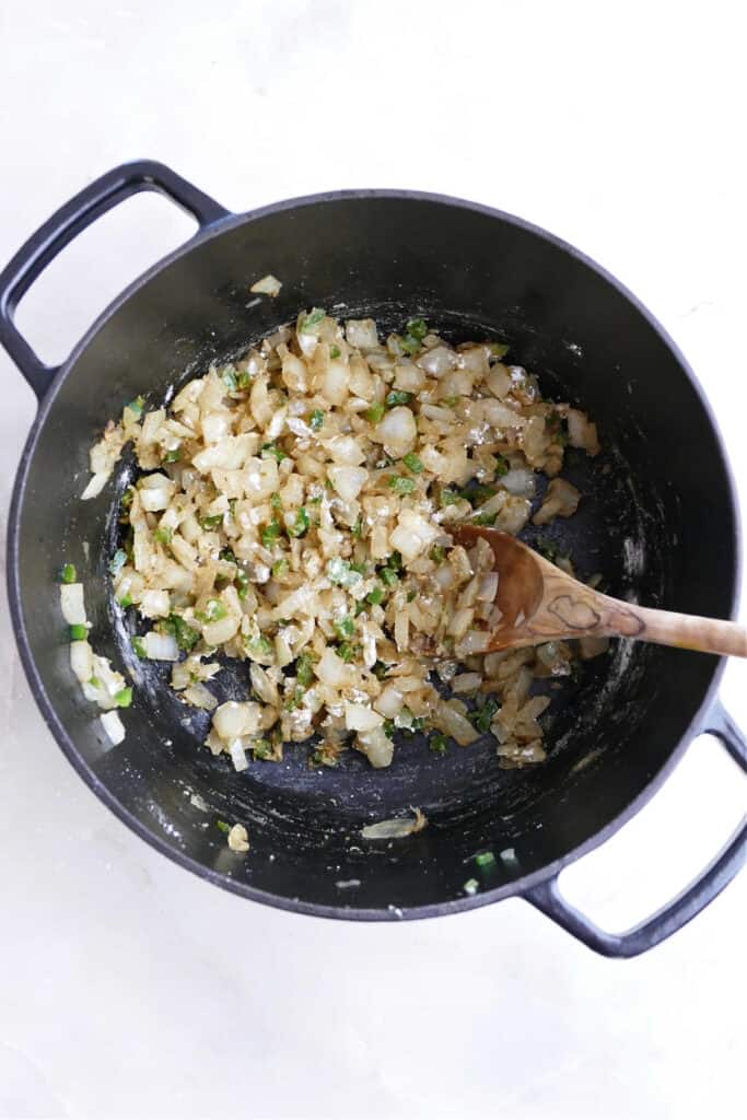 onion, jalapeno, and seasonings cooking in a large pot with a wooden spoon