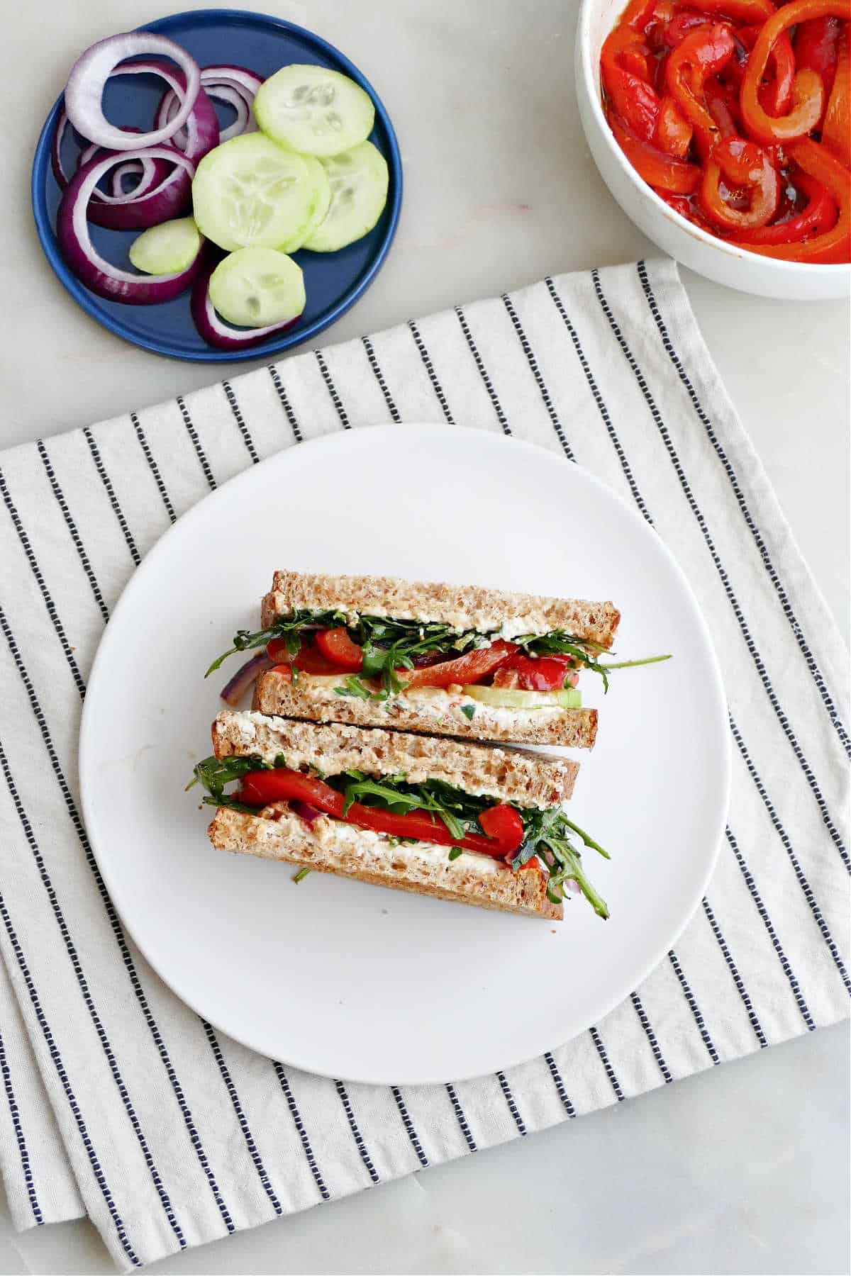 veggie cheese sandwich on a plate on a napkin next to bowls of toppings