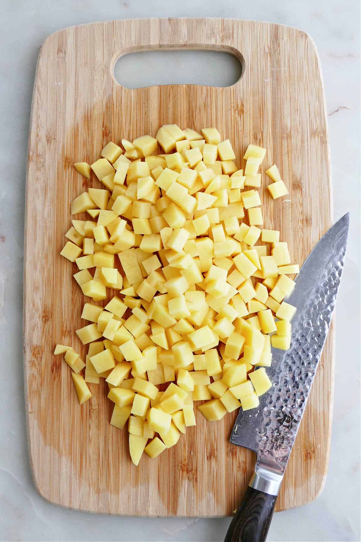 potatoes cut into small cubes on a cutting board next to a chef's knife
