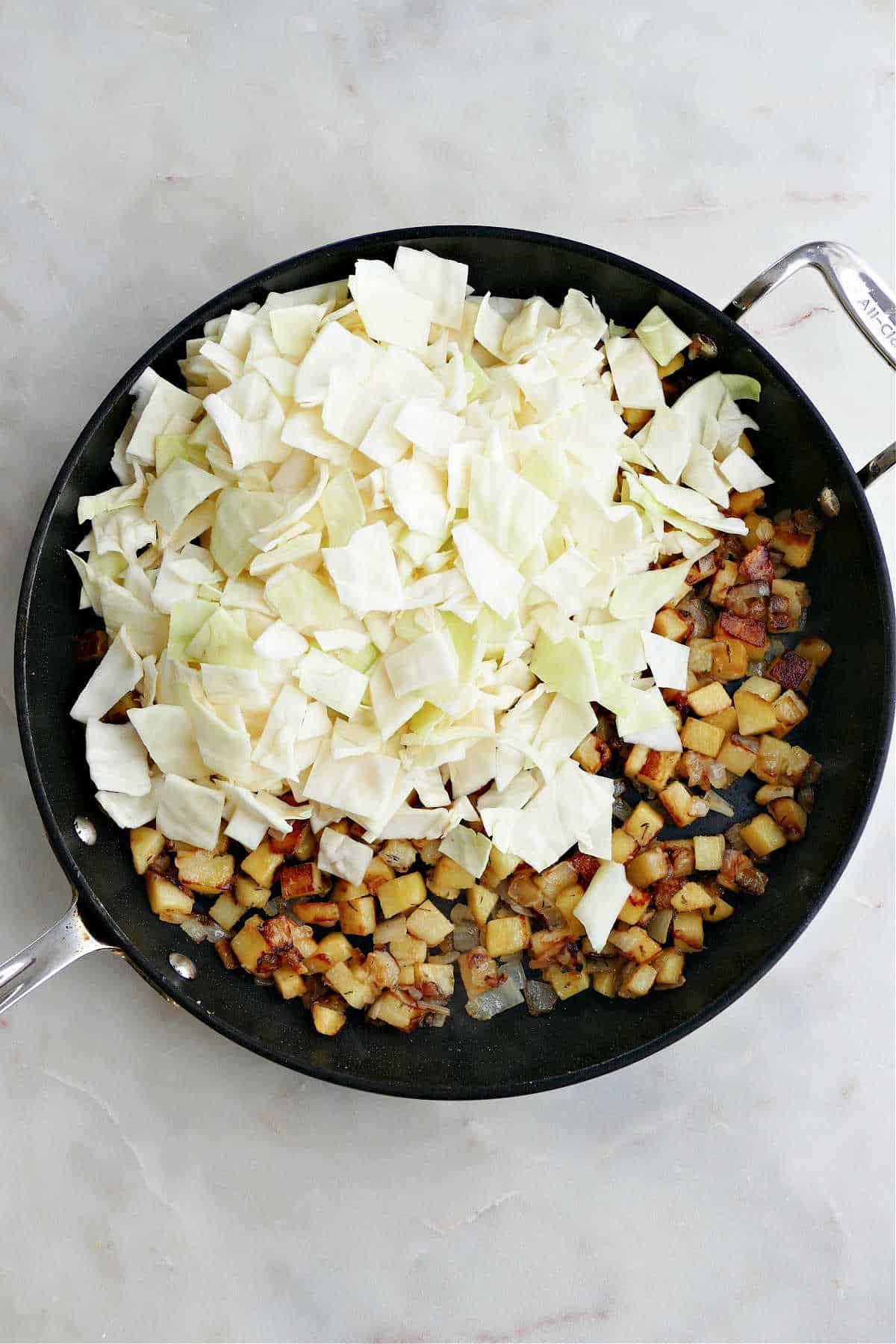 cubed potatoes, sliced cabbage, and onions cooking in a skillet on a counter