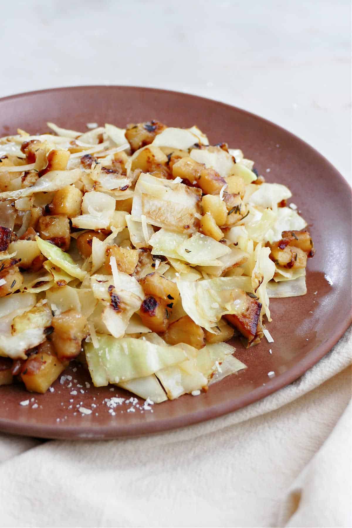 fried cabbage and potatoes on a serving plate on top of a napkin