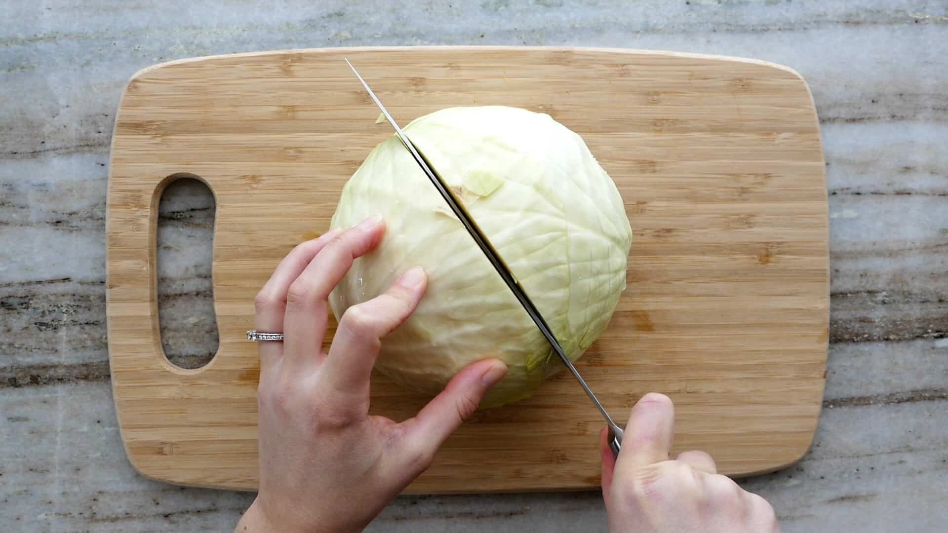 woman cutting a head of cabbage in half with a knife on a cutting board
