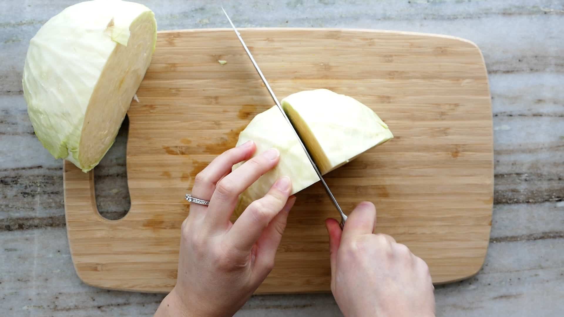 woman cutting a head of cabbage into quarters with a knife on a cutting board