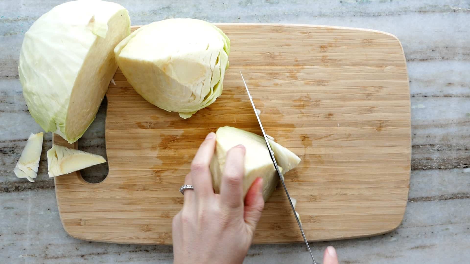 woman slicing off the core from a quarter of cabbage on a cutting board