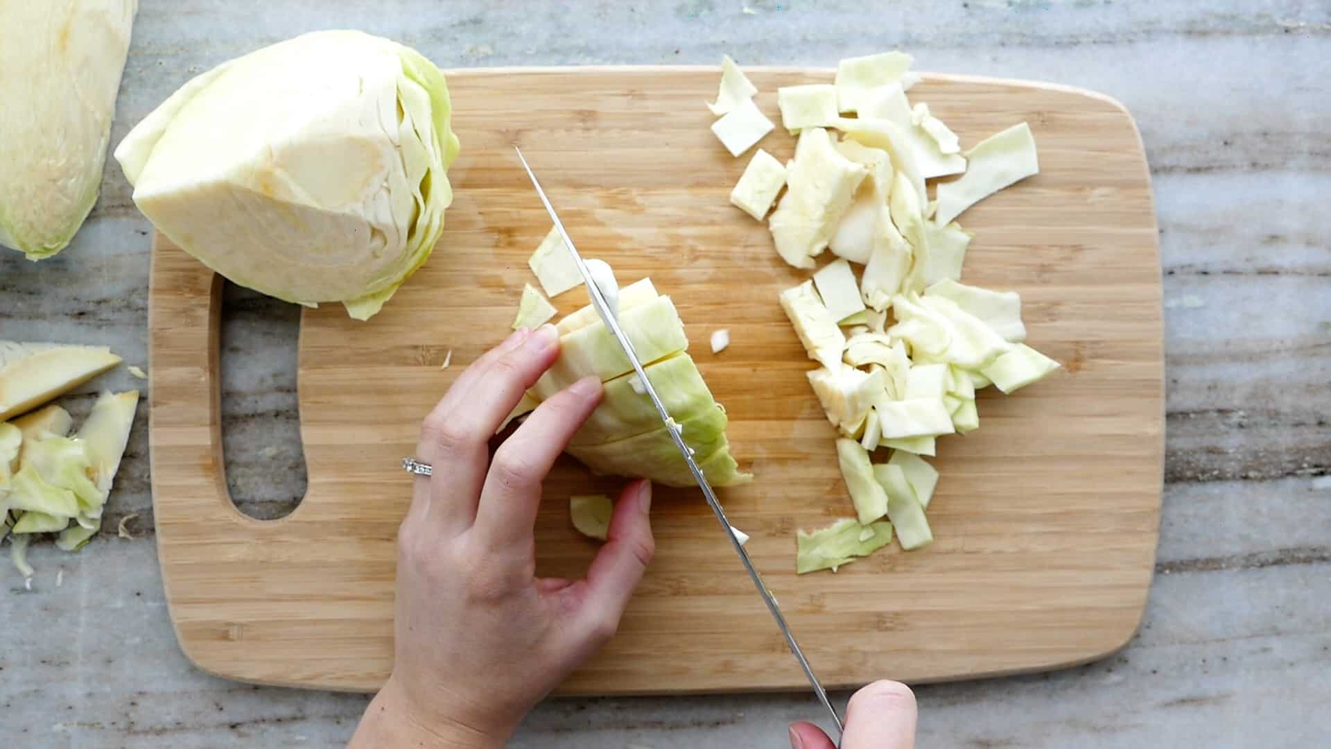 woman dicing cabbage into squares with a knife on a cutting board