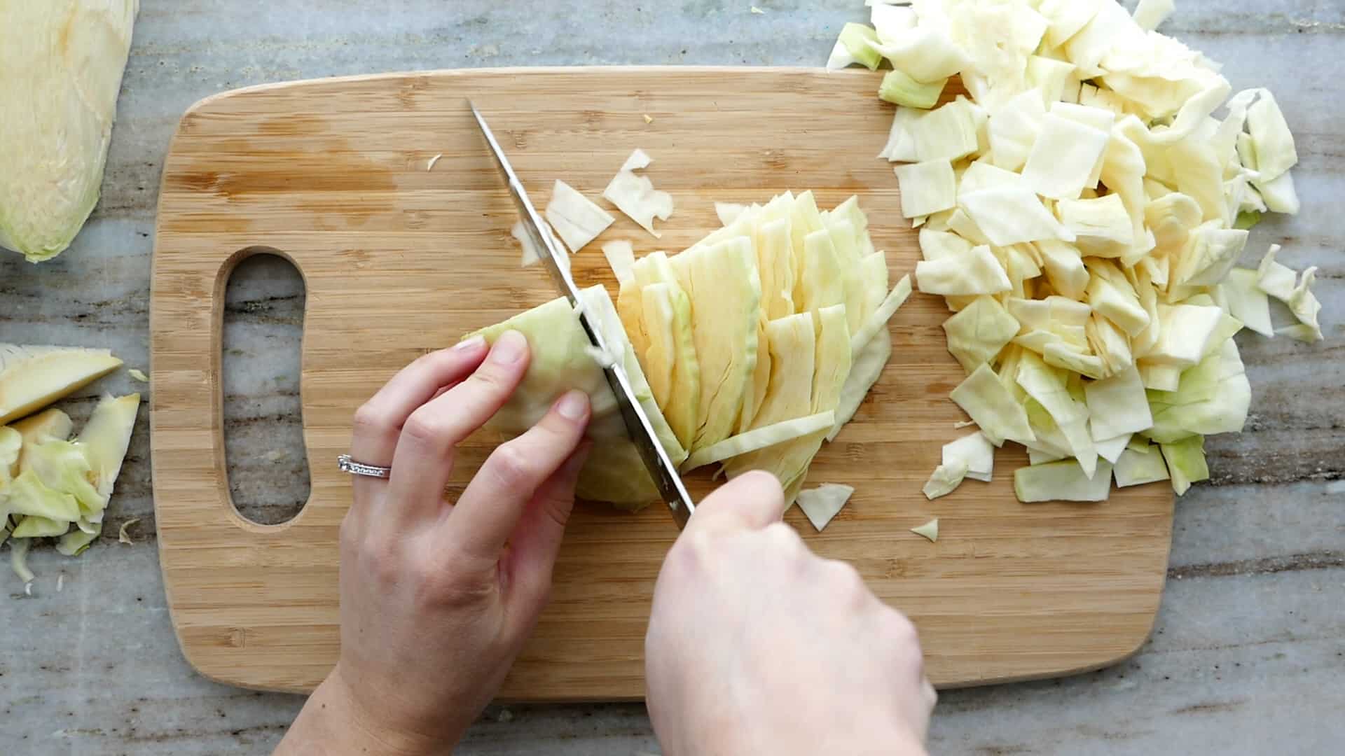 woman cutting cabbage into thin slices on a cutting board with a knife