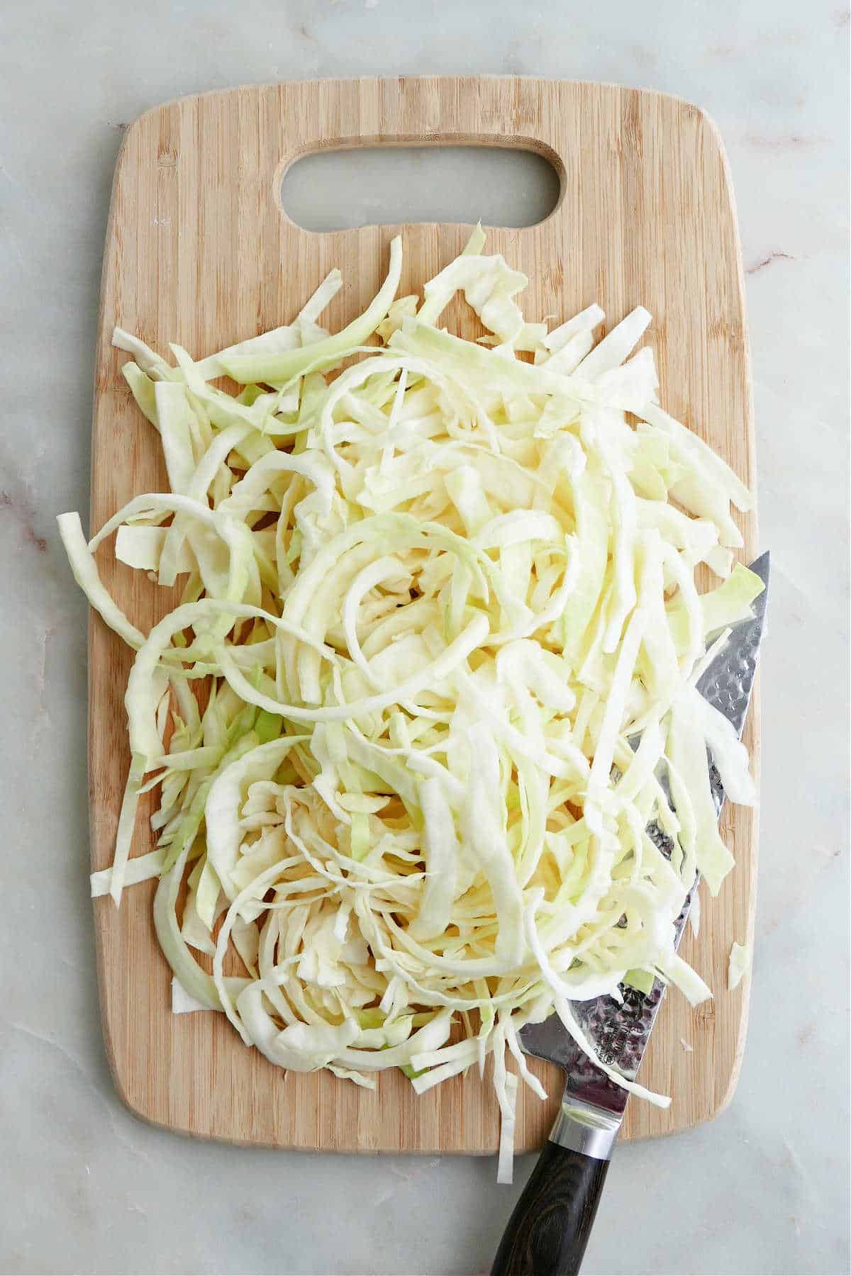 cabbage sliced into thin shreds on a bamboo cutting board with a chef's knife