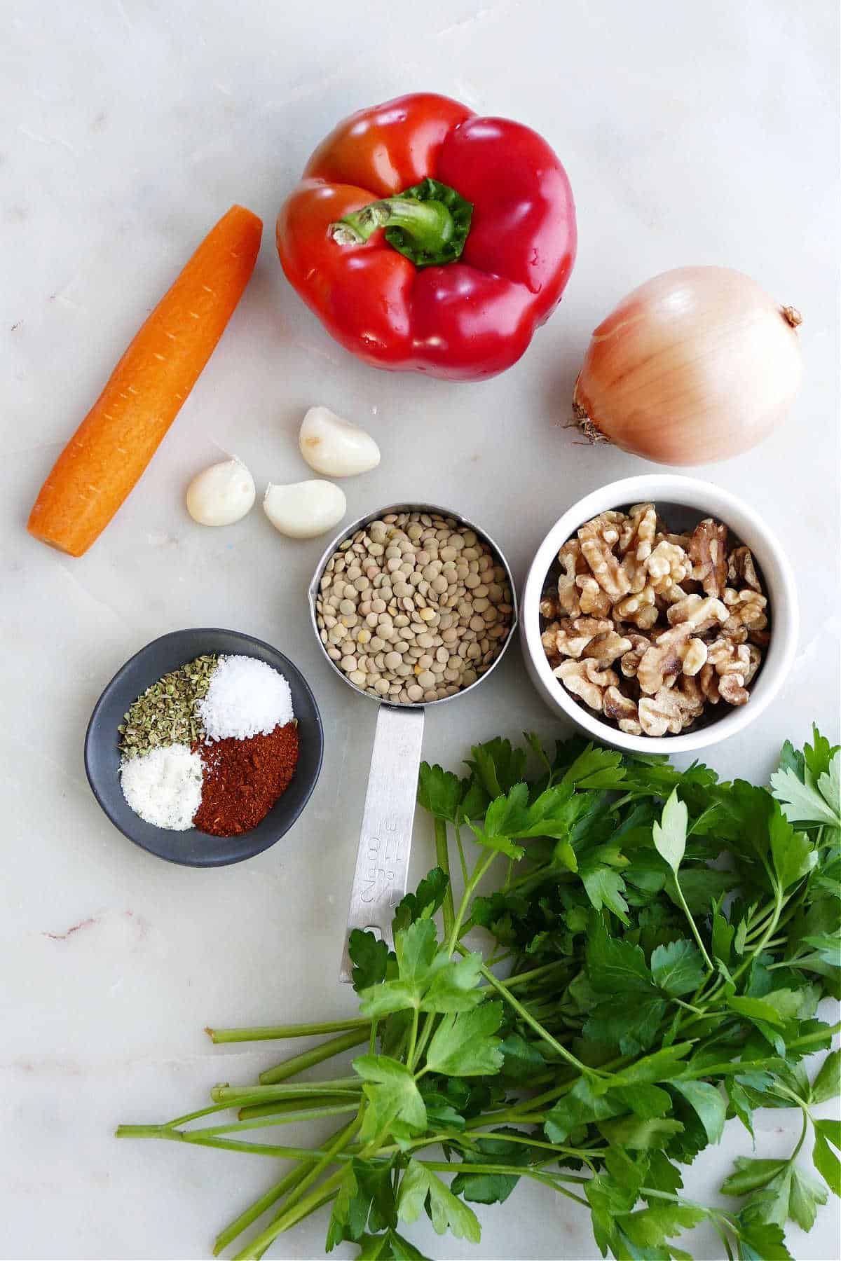 carrot, bell pepper, onion, garlic cloves, walnuts, lentils, seasonings, and parsley on a counter