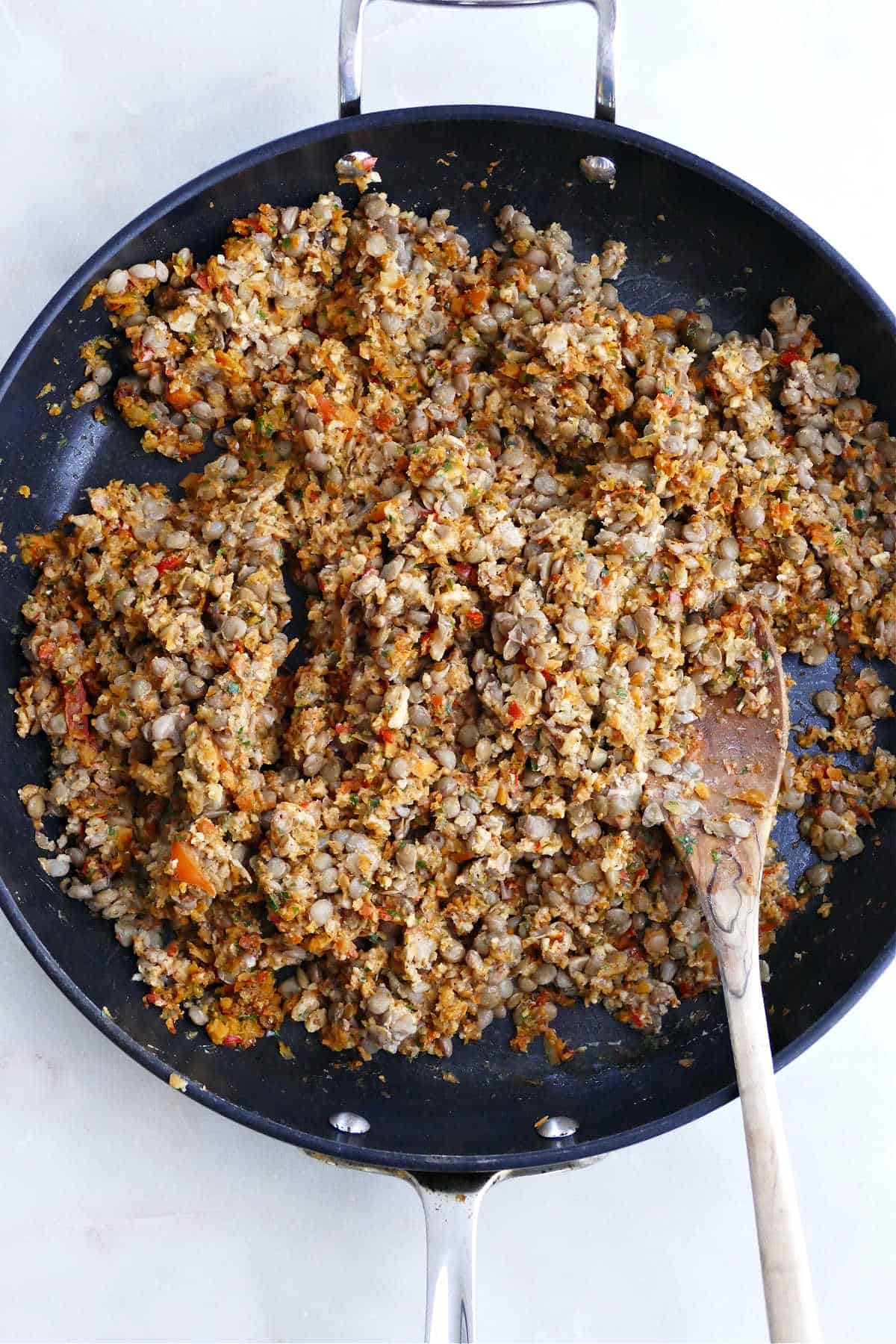 lentil walnut taco meat cooking in a nonstick skillet with a bamboo spoon