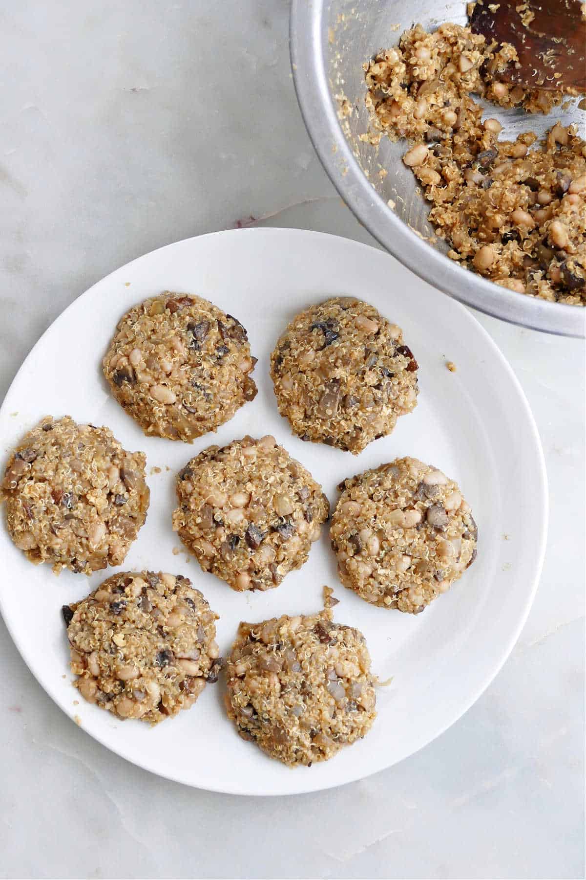 seven quinoa mushroom patties on a plate next to a bowl with the batter